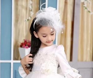 White feather fascinator headband with mesh veil worn by a child in an elegant setting