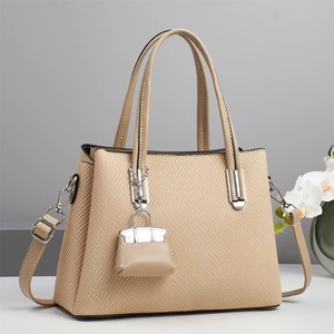 Detail van beige geweven schoudertas met zilveren hardware en een kleine tas-bedeltje