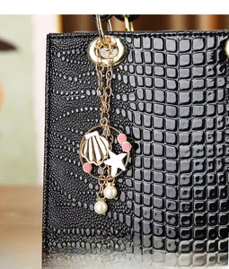 Detail of luxury gold bag charm with shell and pearl accents on black faux croc leather