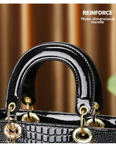 Detail of 3D round handle on black crocodile embossed patent leather tote with gold hardware