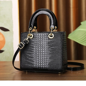 Detail of black crocodile texture bag with gold hardware on a wooden table