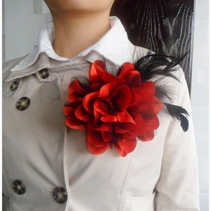 Detail of red fabric flower brooch with black feathers on a beige trench coat