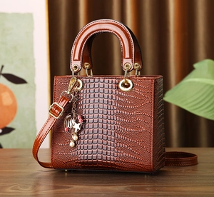 Detailed view of brown crocodile texture handbag with pearl charm and gold hardware