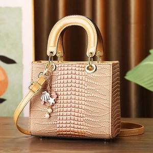 Brown crocodile embossed handbag with pearl sea charm on a warm textured wooden surface