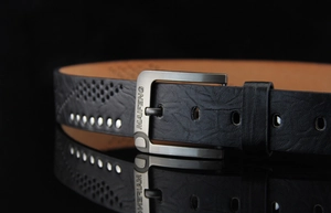 Detail of vintage black leather belt featuring metal rivets and an embossed texture buckle