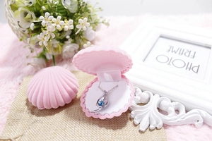 Pink shell-shaped jewelry box holding a silver necklace with a blue gemstone detail