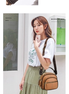 Detail view of caramel brown saddle bag with clover pattern strap and multiple zippers