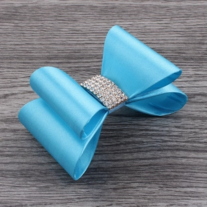 Detail of bright blue satin bow hair clip with sparkling rhinestone center on wood