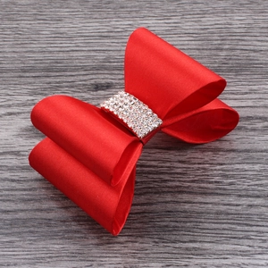 Macro shot of a red satin bow hair clip with sparkling silver rhinestones on a wooden background