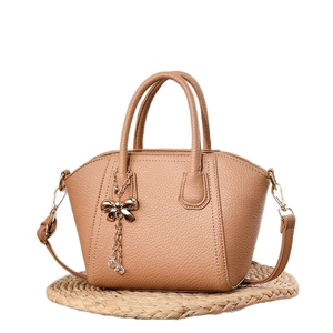 Brown lychee pattern faux leather handbag with golden bow charm on a straw mat background