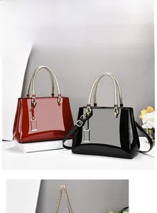 Detail of high-gloss patent leather tote bags with woven gold handles and charms