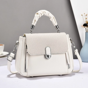 Elegant white crossbody bag with textured flap and silver metal twist lock in indoor setting