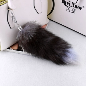 Detail of extra large grey fox fur tail keychain with silver metal clip on white bag