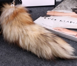 Detail of a large fluffy brown fox fur keychain with a silver clip on a grey surface