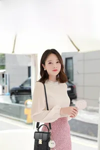Outdoor street view of a small black faux crocodile skin bag with golden clasp and pompom