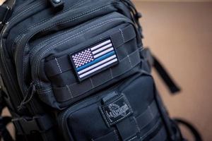 Detail of black tactical backpack featuring MOLLE webbing and Thin Blue Line USA flag patch