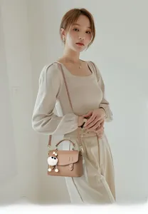Détail d'un petit sac bandoulière en cuir marron avec pompon blanc et boucles dorées