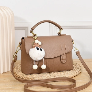 Sac bandoulière marron texture litchi avec breloque peluche sur table en bois