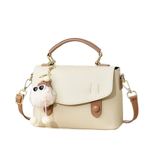 Sac bandoulière beige chic avec poignées marron et charme de monstre en peluche sur fond blanc