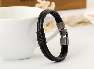 Detail of black leather braided bracelet with vintage grey metal clasp on white cup