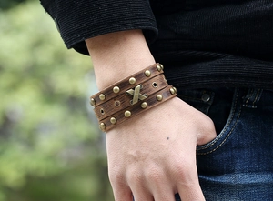 Nahaufnahme eines braunen Lederarmbands im Punk-Stil mit Nieten und X-förmigem Metall-Dekor