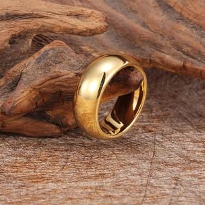 Polished gold tungsten ring hanging on a natural wooden branch with a textured background