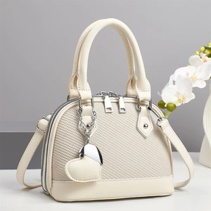 Elegant beige woven shell handbag with heart charm and crossbody strap on white platform