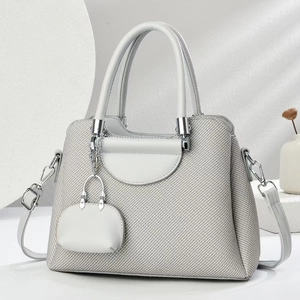 Close-up of light grey tweed handbag with leather trim and matching mini charm pendant