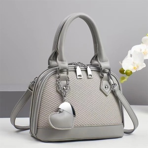Close-up of grey shell bag with dual zippers, heart pendant, and leather texture