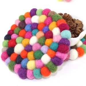 Close-up of handmade colorful wool felt ball coaster beside small bowl of coffee beans