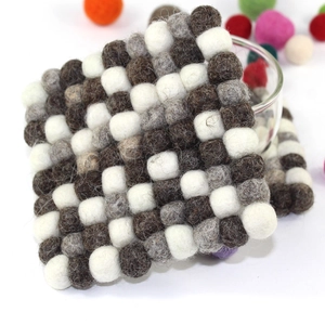 Detail of square handmade felt coasters in white and brown wool balls on white backdrop