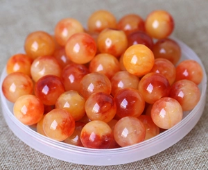 Close-up of orange and white natural agate beads in a transparent bowl on beige fabric