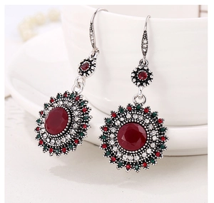 Close-up of vintage sunflower earrings with red gemstones hanging on a white ceramic cup