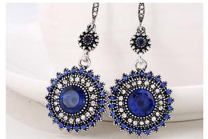 Macro shot of silver sunflower earrings featuring deep blue center gemstone and rhinestones