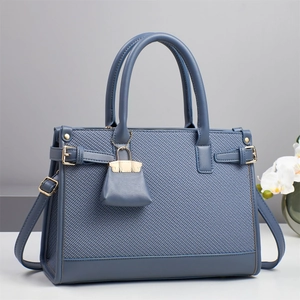 Detail of elegant navy blue handbag with woven texture, golden hardware and charm