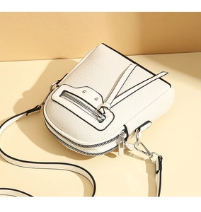 Close-up of off-white textured leather crossbody bag with black trim and silver zipper hardware