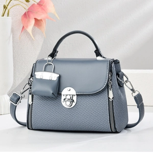 Sac bandoulière bleu-gris texturé avec fermoir rotatif argenté et mini breloque
