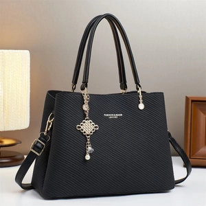 Gros plan détaillé du sac bandoulière noir avec texture sergé et pendentif perle dorée