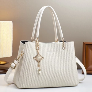 Détail du sac crème texturé avec pendentif nœud doré et perle élégante