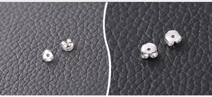 Macro detail of 925 sterling silver butterfly earring backs on black leather background