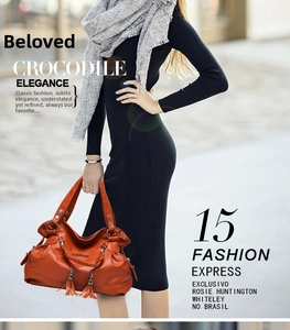 Detailed view of bright orange pebbled leather handbag with side tassels and woven handles