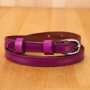 Close-up of purple leather slim belt with silver buckle and wave stitching on wood