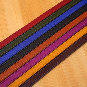 Selection of colorful leather belts with woven texture on a light wood background