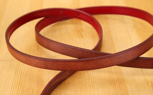 Close-up of slim dark brown leather belt featuring a contrasting red inner lining