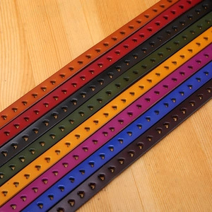 Detail of colorful hollow heart-punched leather belts displayed on a natural wood background