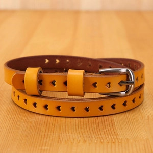 Detail of yellow leather belt with heart-shaped cutouts and silver metal pin buckle