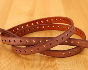 Detailed macro of brown leather belt featuring unique heart-shaped laser cutouts on wood
