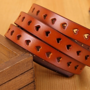Detail view of brown leather belt featuring laser-cut heart patterns on wood surface