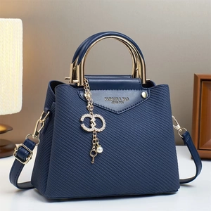 Detail of navy blue crossbody bag with gold three-ring handle and rhinestone pendant