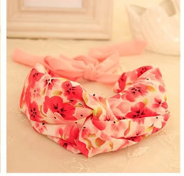 Detail of baby pink floral headband with soft bow resting on neutral fabric